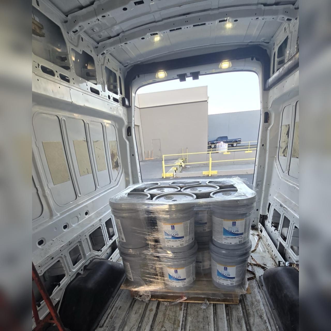 Interior of an empty van with a pallet of stacked paint buckets inside.