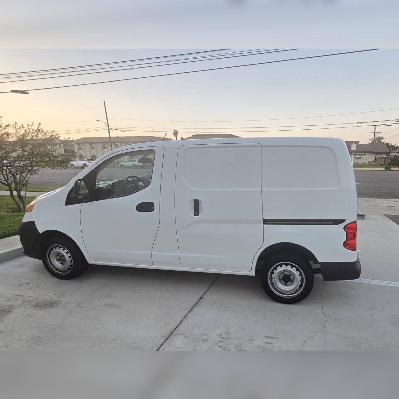 Side view of a white cargo van parked in a residential driveway at sunset.