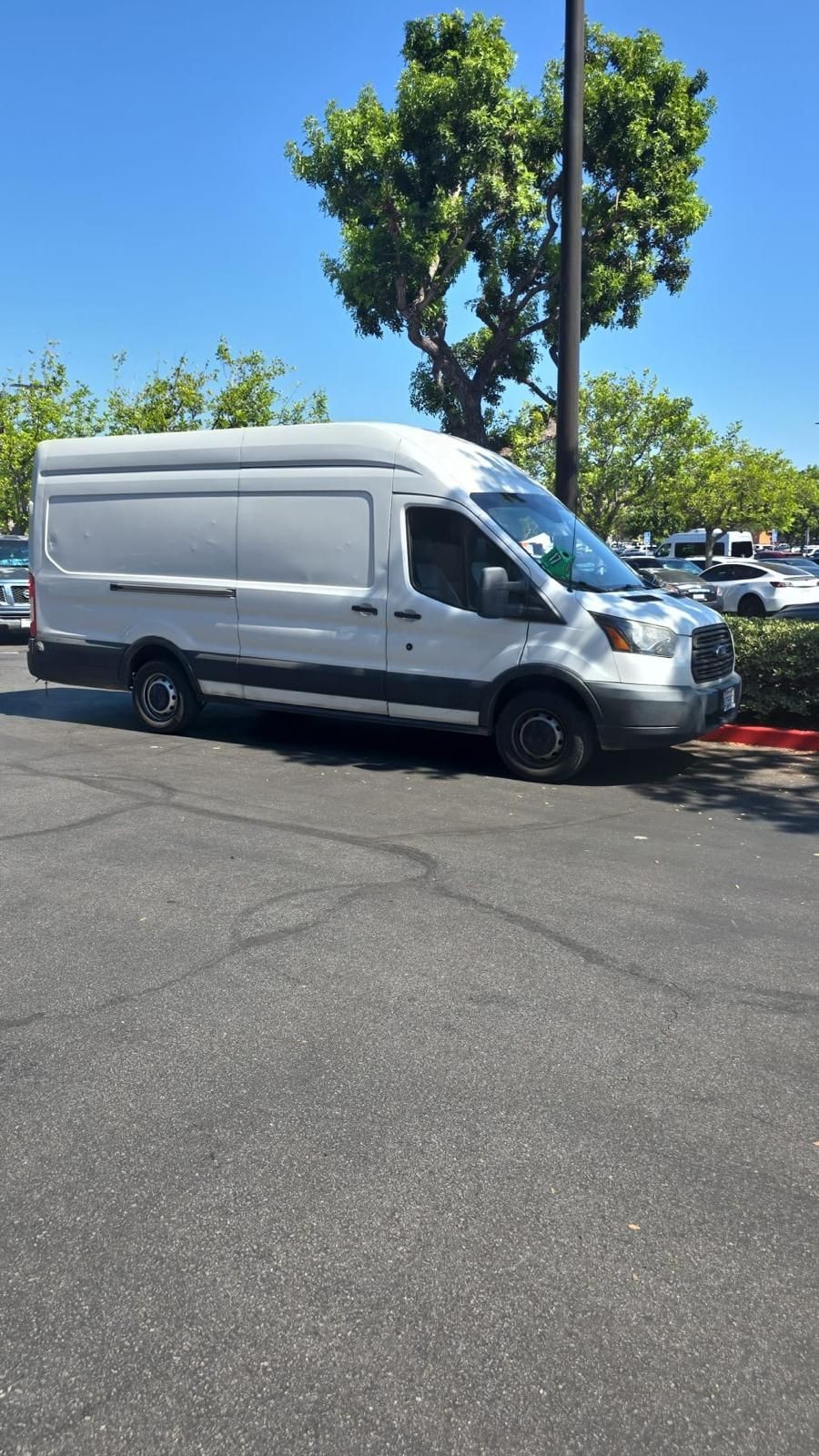 White delivery van parked on asphalt near trees under clear blue sky.